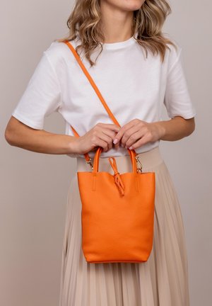 Kleine orangefarbene Lederhandtasche mit einer genarbten Textur, zwei kurzen Griffen und einem abnehmbaren Umhängegurt. Hält ein Knotendetail oben.