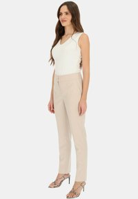 Biały top bez rękawów z dekoltem w serek, w połączeniu z jasnobeżowymi, dopasowanymi spodniami oraz sandałami na wysokim obcasie z zapięciem, zdobionymi wzorem.