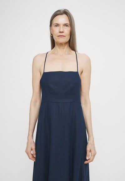 Robe en lin bleu marine avec des bretelles fines, un décolleté droit et une jupe fluide. Présente une texture lisse et des lignes de design simples.