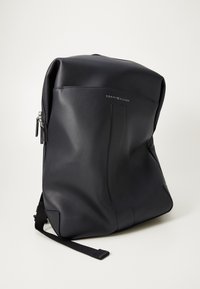 Black leather backpack with minimalistic design, featuring a smooth texture, a zip closure, and a logo accent on the front.