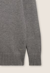 Maglione grigio a maglia caratterizzato da polsini e orlo a coste, realizzato in un tessuto morbido con una superficie texture. Piccola etichetta con logo in basso a sinistra.