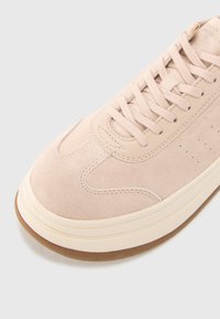 Sneaker in suede rosa chiaro con punta arrotondata, cuciture sottili, design con lacci e suola in gomma beige. Presenta piccole perforazioni ai lati.