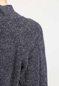 Mörkblå, strukturerad stickad tröja med hög hals. Har en lös passform och mjukt, fluffigt material som ger ett mysigt och varmt intryck.