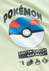 Vihreä puuvillapaita, jossa on sininen ja punainen Pokéball-grafiikka, ylhäällä teksti "POKÉMON" ja alhaalla mustalla "GOTTA CATCH 'EM ALL!".