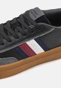 Baskets en cuir noir et daim gris avec des bandes bleu marine, rouge et blanche. Semelle en caoutchouc arrondie avec des détails texturés et lacets plats.