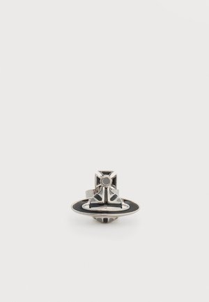 Anillo plateado y negro con un diseño de cruz y orbe circular sobre un fondo blanco liso.