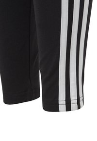 Pantaloni sportivi neri con strisce verticali bianche sui lati; il tessuto sembra liscio e traspirante, con una vestibilità comoda all'orlo.