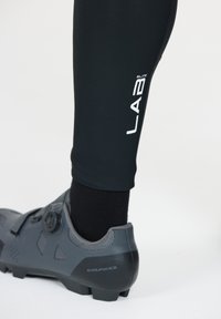 Svarta cykelleggings med tajt passform, med en vit "LAB"-logotyp. En svart cykelsko med övre del i grått mesh och en rattstängning visas.