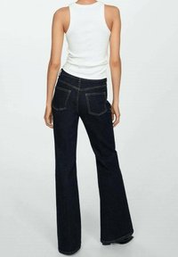 Los pantalones de mezclilla acampanados de color azul oscuro presentan una cintura alta, dos bolsillos traseros y costuras en contraste. El material parece resistente y tiene una textura suave.