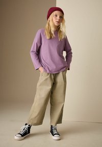 Long-sleeve lavender t-shirt, loose-fitting beige trousers, black high-top sneakers with white soles, and a maroon knitted beanie.