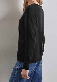 Svart stickad tröja med långa ärmar, rund halsringning och ribbade muddar, i kombination med blå denimjeans. Slät textur och åtsittande design.