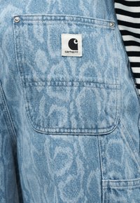 Ανοιχτό μπλε τζιν ύφασμα με υφή. Διαθέτει λογότυπο σε τετράγωνο πατς και πλαϊνή τσέπη με κουμπί.