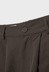 Cintura di pantaloni marrone scuro con chiusura a bottone e passanti per cintura, che mostrano cuciture dettagliate e trama del tessuto.