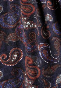 Ciemna tkanina z wzorem paisley w kolorach czerwonym, niebieskim, białym i czarnym, z misternymi detalami kwiatowymi oraz teksturowaną powierzchnią.