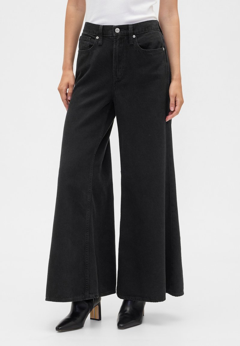 Jeans pretos de perna larga feitos de ganga, com cintura alta, dois bolsos frontais e acabamento desgastado. Combinados com saltos pretos pontiagudos.