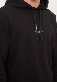 Sweat à capuche noir en tissu mélangé coton, avec une poche kangourou, des cordons de serrage et un petit logo imprimé sur la poitrine.