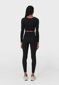 Svart ribbad crop top och tights, figurnära design med långa ärmar, kombinerat med ljusa träningsskor med svart accent.