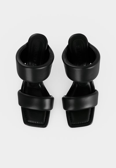 Μαύρα σανδάλια ανοιχτής μύτης με επενδεδυμένους πλατιούς ιμάντες πάνω από τα δάχτυλα και τους αστραγάλους, και τετράγωνο σχέδιο μύτης, φαινομενα από πάνω σε λευκό φόντο.