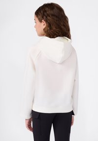 Sudadera blanca con una textura suave, un forro en contraste de color claro en la capucha y mangas de corte holgado, combinada con pantalones cargo negros.