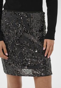 Fekete flitteres mini szoknya, testhez simuló kialakítással, sima tapintással és fényes flitterekkel, amelyek függőleges mintázatban helyezkednek el.