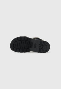 Black rubber shoe sole features textured pattern with deep grooves and "COACH" logo embossed for traction and branding.