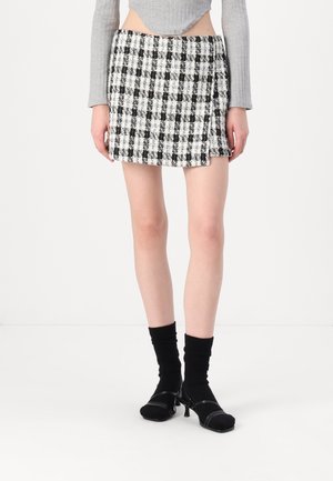 Kvinde iført sort-hvidternet mini nederdel, grå langærmet cropped top, sorte sokker og sorte remsandaler med hæl.