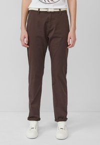 Chinos en coton marron avec une ceinture tissée crème, design à jambes droites et ourlets retroussés, associés à des baskets blanches.