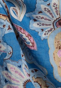Blumiger Baumwollstoff mit blauer Hintergrundfarbe und komplexen weißen, rosa und braunen Mustern, die eine strukturierte Oberfläche aufweisen.