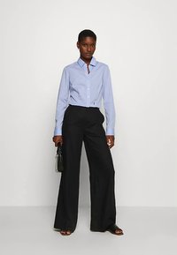 Light blue long-sleeve shirt with a button-down collar paired with high-waisted black wide-leg trousers. The look is complemented by a small black bag.