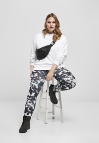 Felpa bianca, leggings neri con tie-dye, borsa a tracolla nera e stivali neri. Tessuto morbido con una vestibilità rilassata e motivi distintivi.