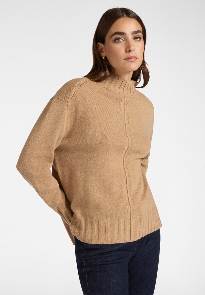 Beige polokrage tröja med ribbad nederkant, strukturerad design och sidofickor. Tillverkad av mjukt tyg med en slät yta.