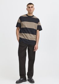 Camiseta de rayas en azul marino y marrón claro, hecha de algodón. Corte holgado, mangas cortas, escote redondo. Combina con pantalones oscuros y zapatos negros.