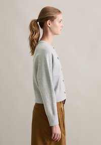 Ljusgrå stickad cardigan med rund halsringning, knappdetaljering framtill och ribbade ärmslut, kombinerad med bruna kordfläskbyxor.