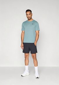 Gaiši zils svītrains īsroku krekls kopā ar tumšiem šortiem. Uz krūtīm ir redzama logotips, valkā baltas sporta apavi ar potīšu zeķēm.