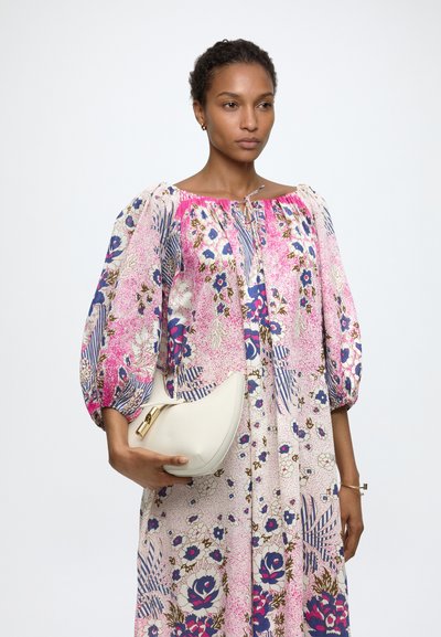 Mujer con un vestido floral rosa, azul y blanco con mangas abullonadas, sosteniendo un bolso blanco de media luna con un broche dorado.