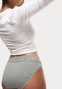 Mutandine verdi a pois con un dettagli in pizzo in vita, tessuto morbido, design a vita alta e superficie liscia, abbinate a un top grigio chiaro.