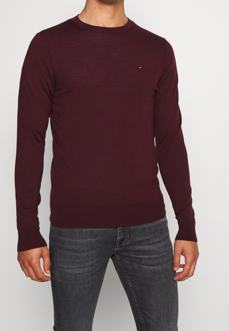 Bordeauxroter Pullover mit langen Ärmeln aus weichem Material, mit Rundhalsausschnitt und einem kleinen Logodetail auf der Brust.