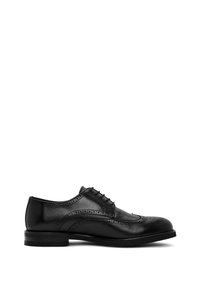 Zapato brogue de cuero negro con detalles en punta de ala, perforaciones y cordones cerrados, mostrado en una vista lateral sobre un fondo blanco.