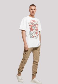Hvit bomull t-skjorte med grafisk trykk av Tom og Jerry i rødt, sammen med beige cargo joggebukser og hvite sneakers.