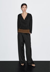 Top nero a V con una fascia marrone testurizzata in vita, abbinato a pantaloni neri larghi. Design semplice, tessuto morbido, vestibilità comoda.
