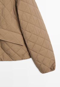 Manche de veste matelassée marron clair avec poignet élastique et poche à rabat sur le côté, présentée sur un fond blanc.