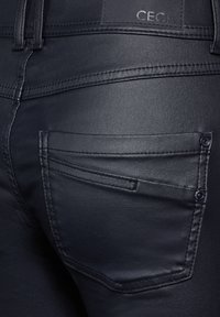 Svarta denimjeans med en slät textur, bakfickor med subtila sömmar och en varumärkesetikett präglad på midjebandet.