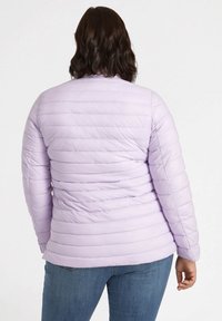 Giacca a vento viola chiaro con trapuntatura verticale e orlo dritto, abbinata a jeans blu. Presenta un colletto alto e maniche lunghe.