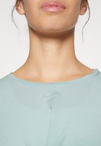 Ljusblå t-shirt med kort ärm gjord av mjukt tyg, med en diskret grå Nike-logotyp på bröstet och rundad halsringning.