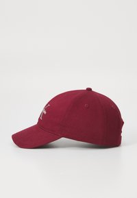 Cască de baseball bordo, realizată dintr-un material moale, cu o visieră curbă, orificii cusute și un logo brodat pe panoul frontal.