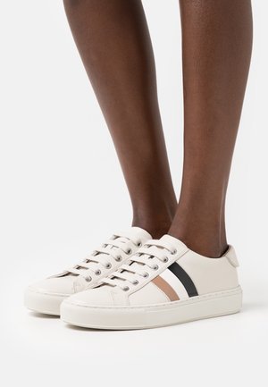 Beige Ledersneaker mit schwarzen und braunen Streifen, rundem Zehenbereich, flacher Sohle und Metallösen. Schnürsenkel zum Binden auf der Vorderseite.