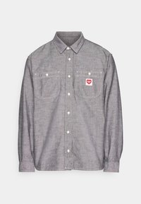 Grijs overhemd met lange mouwen en knopen, twee borstzakken, witte knopen en een rood Carhartt-logo op de rechterborstzak.