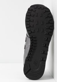 Calzature grigie con suola in gomma nera testurizzata. Presentano un design snodato e una costruzione robusta con cuciture e cinghie visibili.