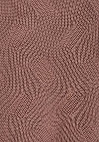 Gros plan sur un tissu tricoté rose poussiéreux avec un motif en zigzag texturé de câbles et des mailles visibles.