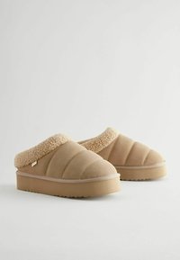 Chaussons beiges à enfiler avec un design matelassé, col en fausse fourrure texturée et semelle en caoutchouc épaisse. Tissu doux et rembourrage garantissant le confort.